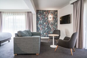 A modern hotel room with a grey sofa, a round table, and a grey armchair. - Holiday Inn Perpignan by IHG (Perpignan)