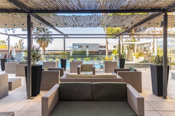 Un área de estar al aire libre con mobiliario de mimbre y una piscina al fondo.