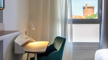 Een hotelkamer met een bureau, een stoel, een lamp, een raam met uitzicht op een gebouw en een bed.