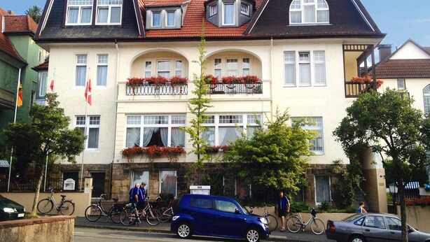 Un edificio de dos pisos con fachada simétrica, múltiples ventanas y balcones decorados con flores rojas.