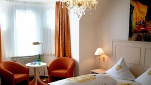 Una habitación de hotel con cama, dos sillones, una mesita, lámpara y candelabro.
