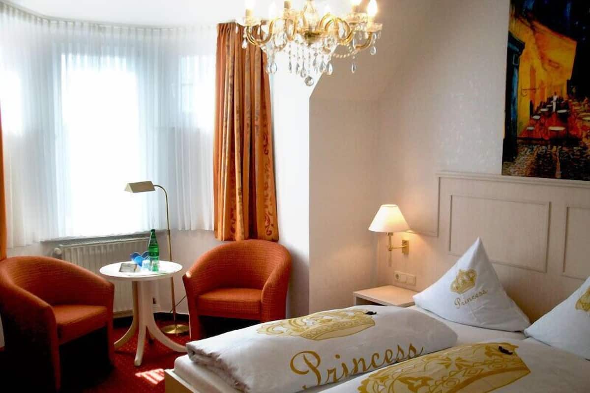 Een hotelkamer met een bed, twee stoelen, een tafeltje, een lamp en een kroonluchter.