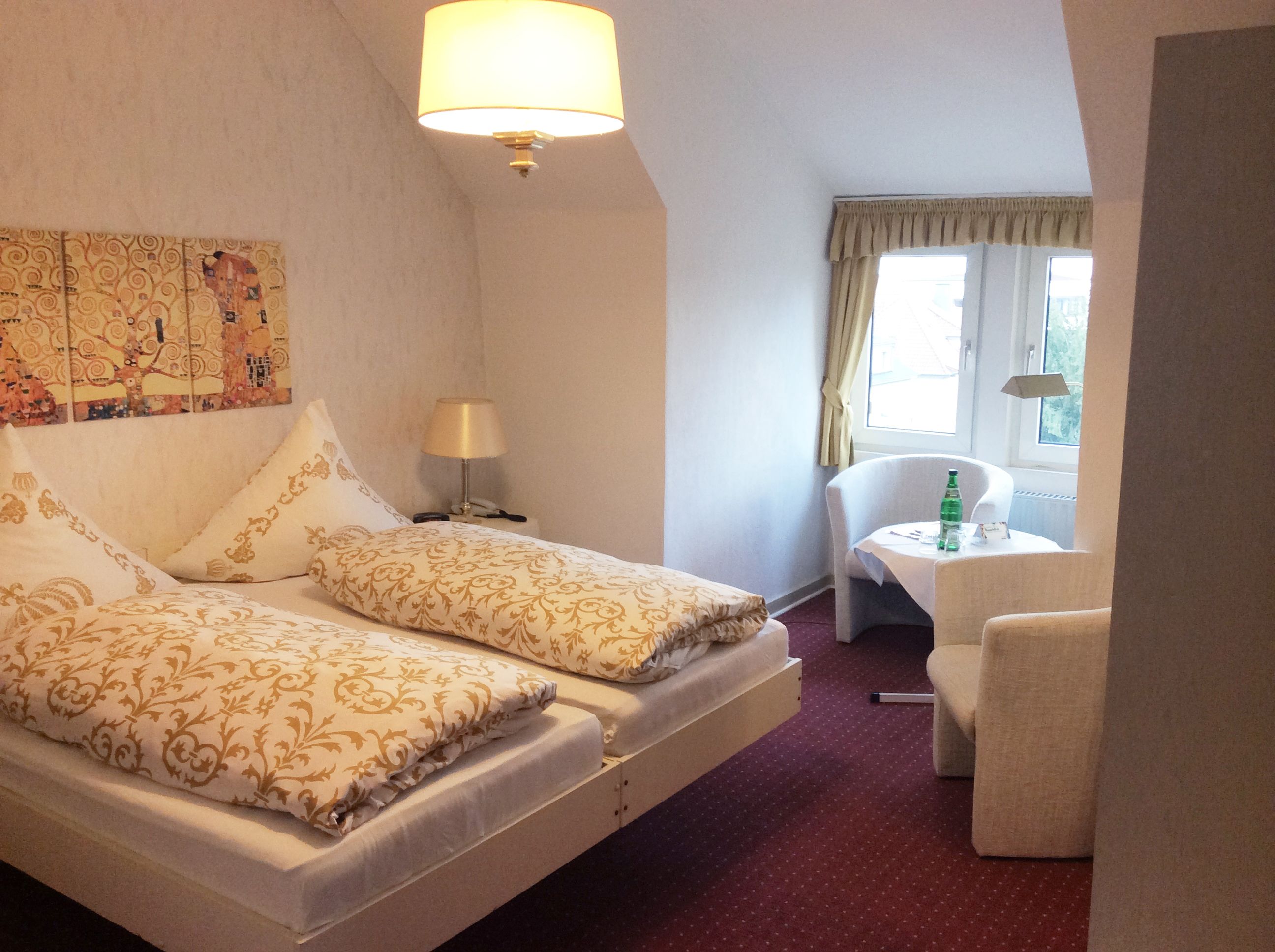 A hotel room with a bed, a small table with a chair, and a window with curtains.