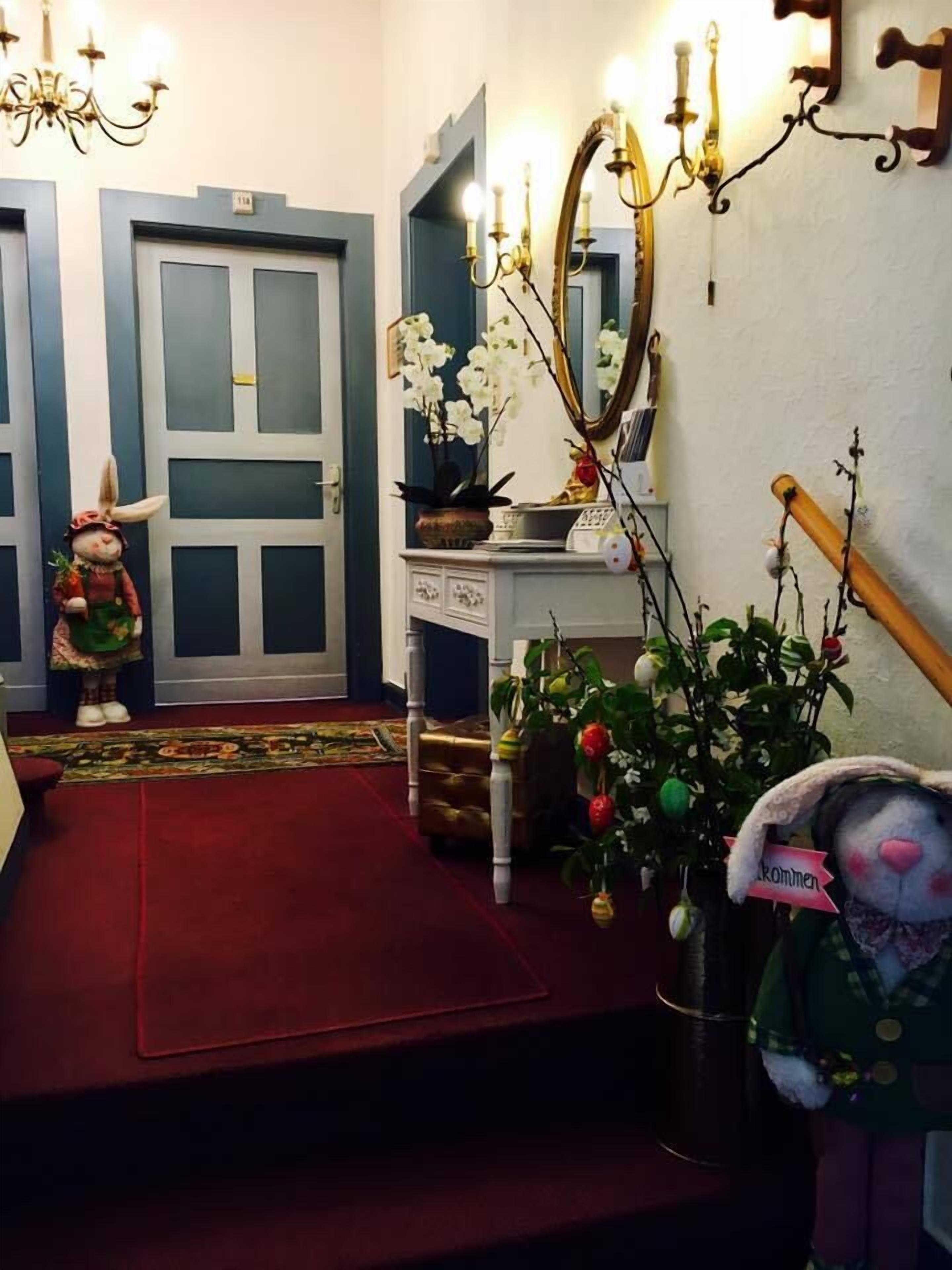Un pasillo con alfombra roja, una consola blanca con espejo, un candelabro y un conejo de peluche.