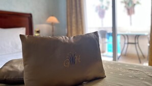 Un lit avec un oreiller orné d’un monogramme et donnant sur un balcon agrémenté de plantes en pot.