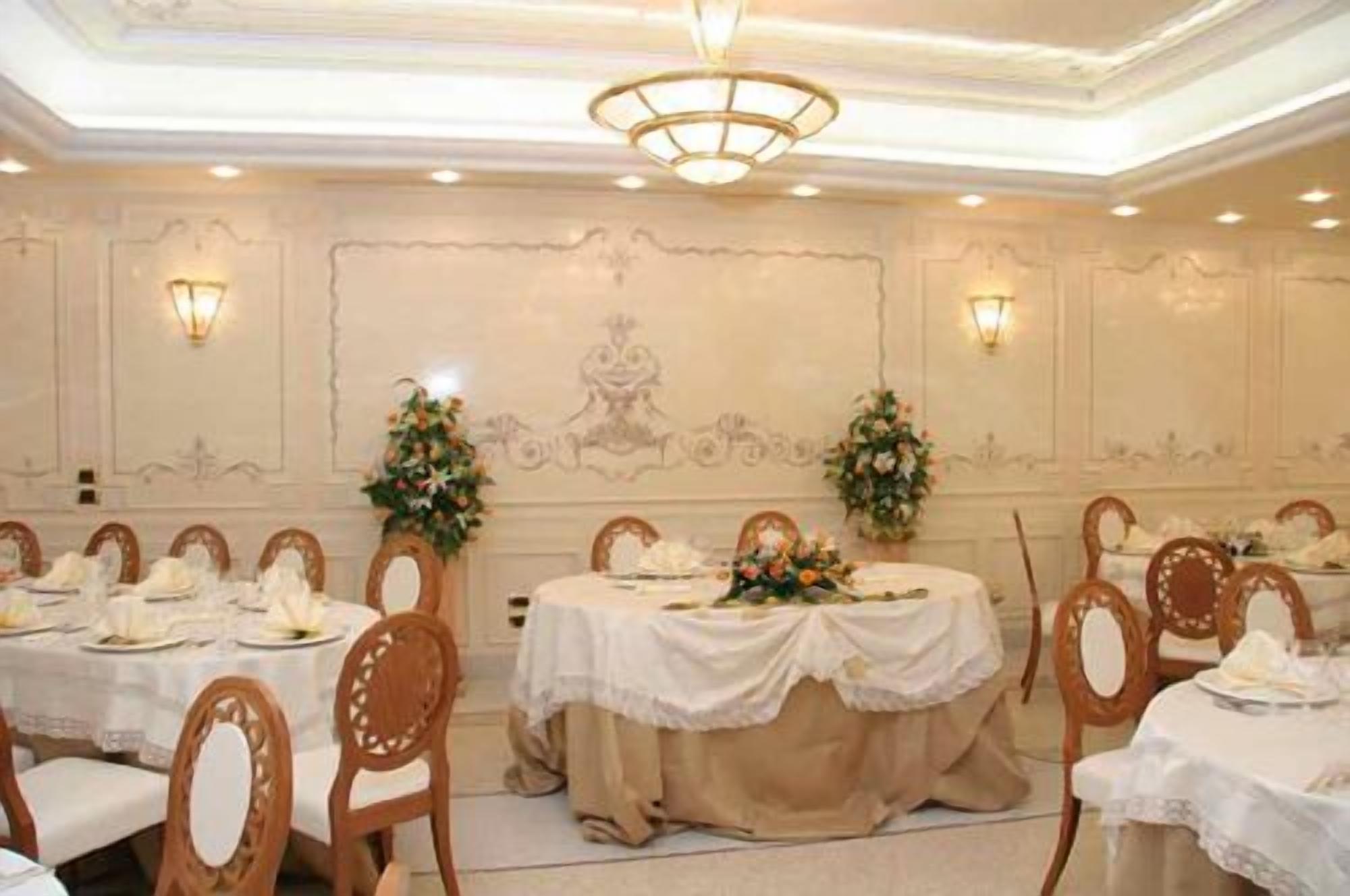 A banquet hall with round tables covered in white tablecloths, wooden chairs, and floral centerpieces.