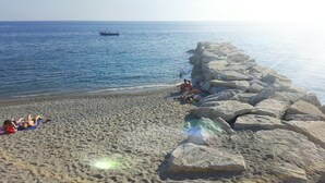 Une plage où des gens se prélassent au soleil, avec une digue rocheuse en arrière-plan.