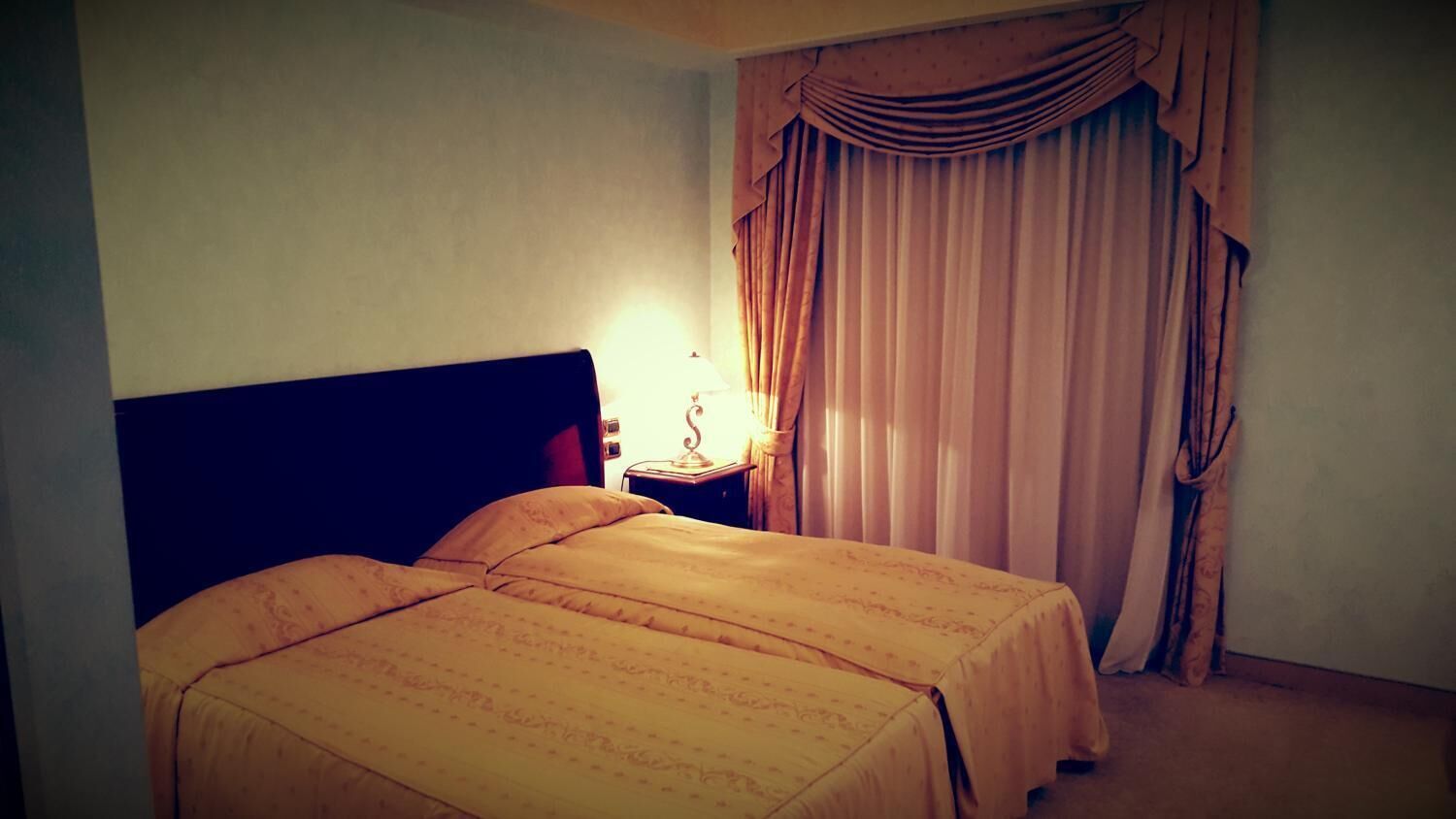 Ein Hotelzimmer mit Doppelbett, Nachttisch mit Lampe und einem Fenster mit Vorhängen.