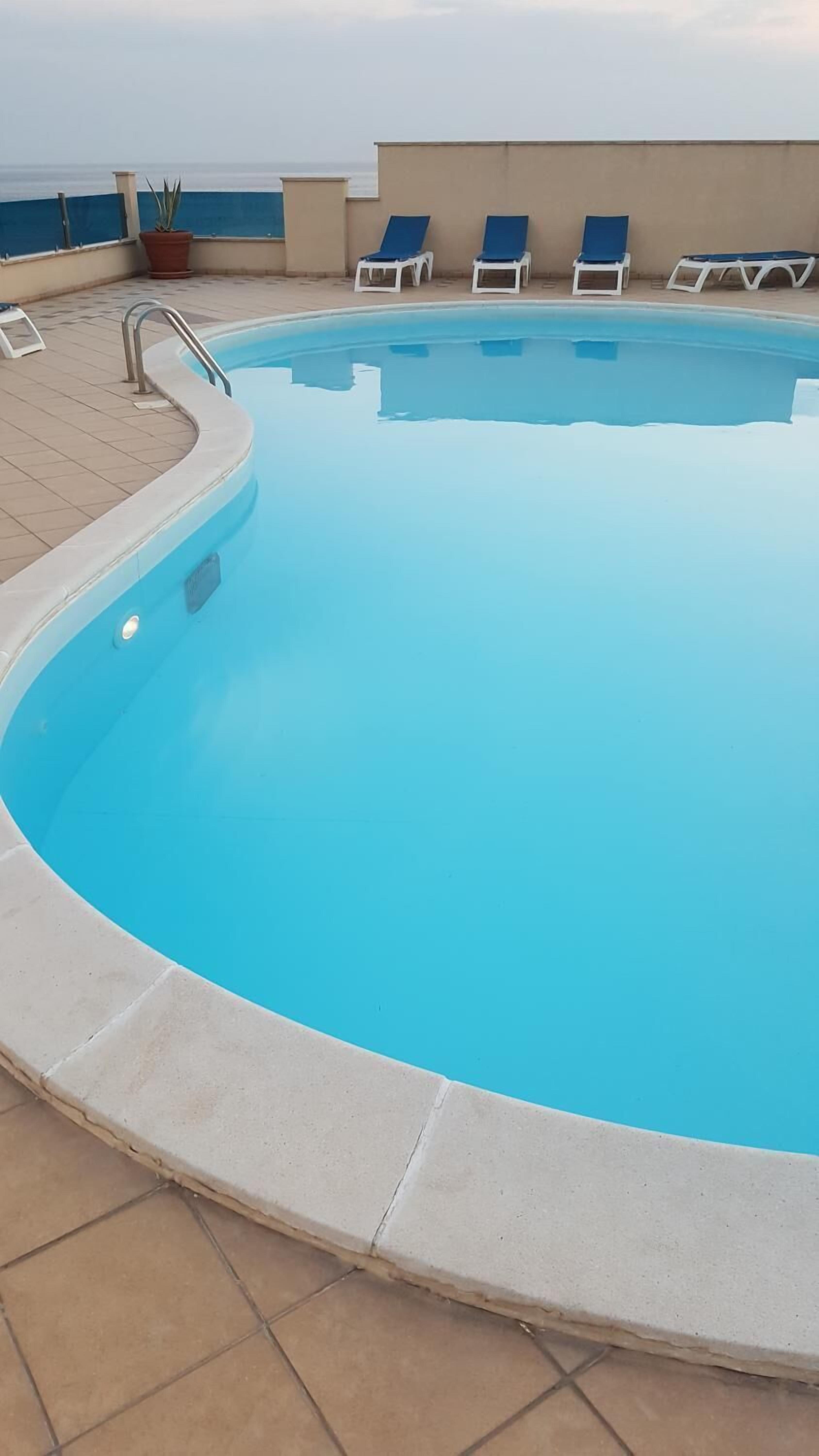 A clear blue pool with a tiled deck, a metal handrail, and several lounge chairs.