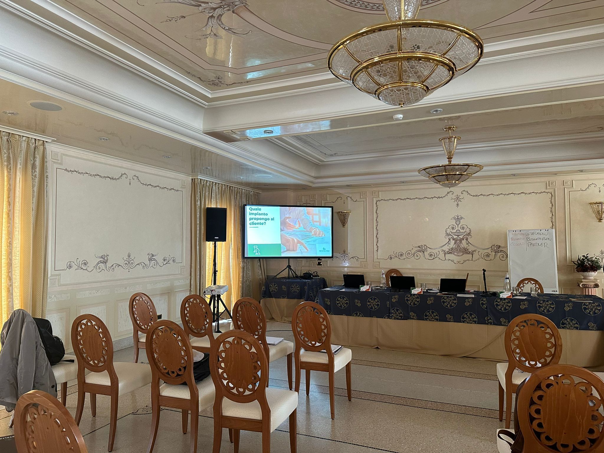 A conference room with a large screen, wooden chairs, a reception desk, and ornate ceiling details.