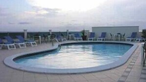 Une piscine sur le toit, avec des chaises longues et un pot de fleurs.