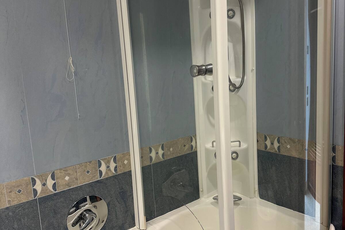 Une douche à l’italienne avec une porte en verre, une baignoire blanche et un sol carrelé agrémenté d’une bordure décorative.