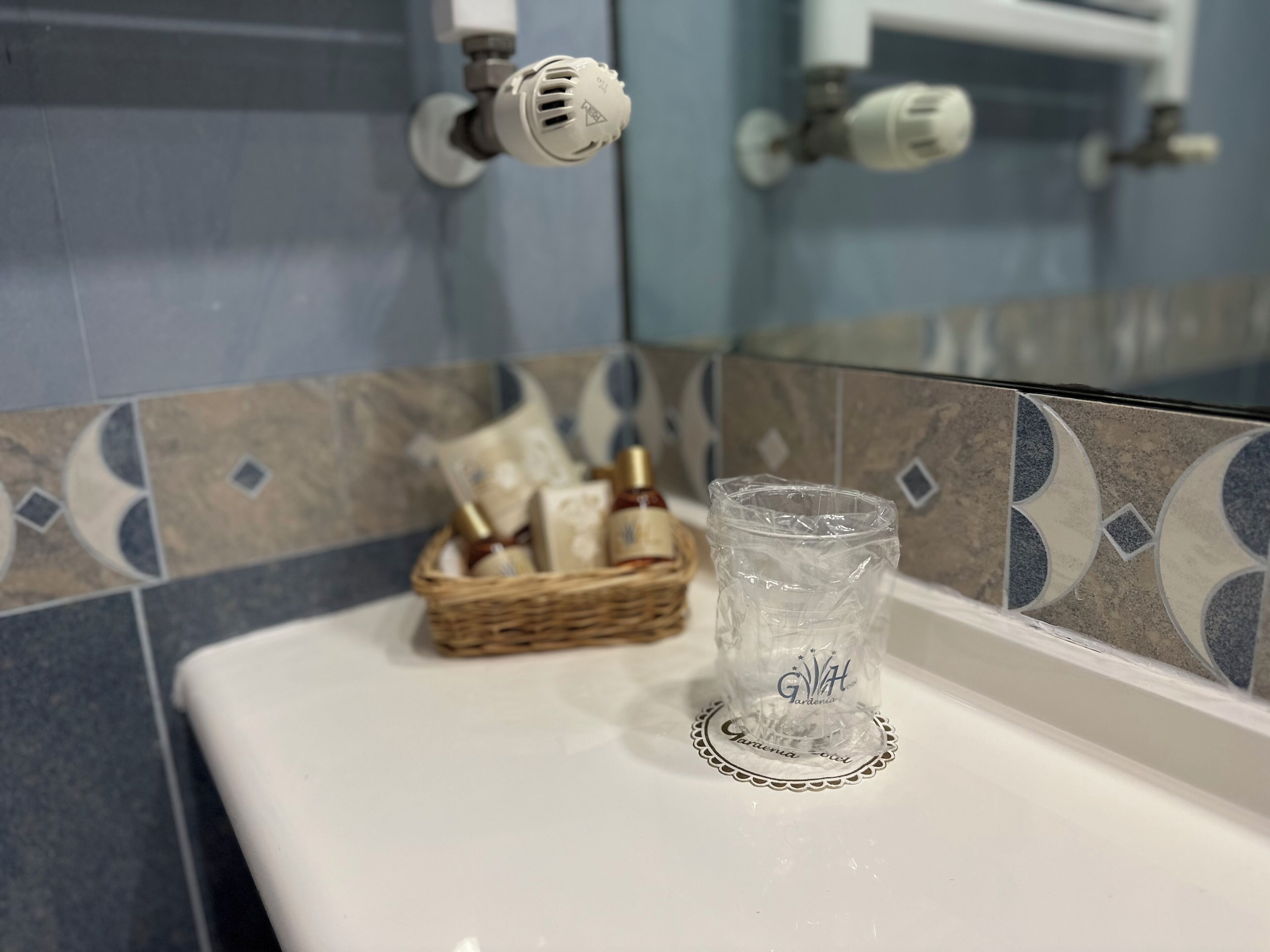 Ett badrum med ett vitt handfat, ett glas och en korg med toalettartiklar.