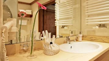 Un baño con lavamanos blanco, espejo y una cesta de mimbre con artículos de aseo.