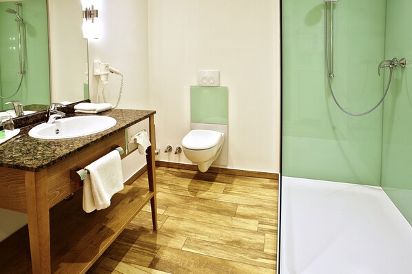 Un baño con tocador de madera, lavamanos blanco y ducha con mampara de vidrio.