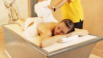 A massage therapy room with a marble massage table, a statue on the wall, and a person in a yellow shirt performing a massage.