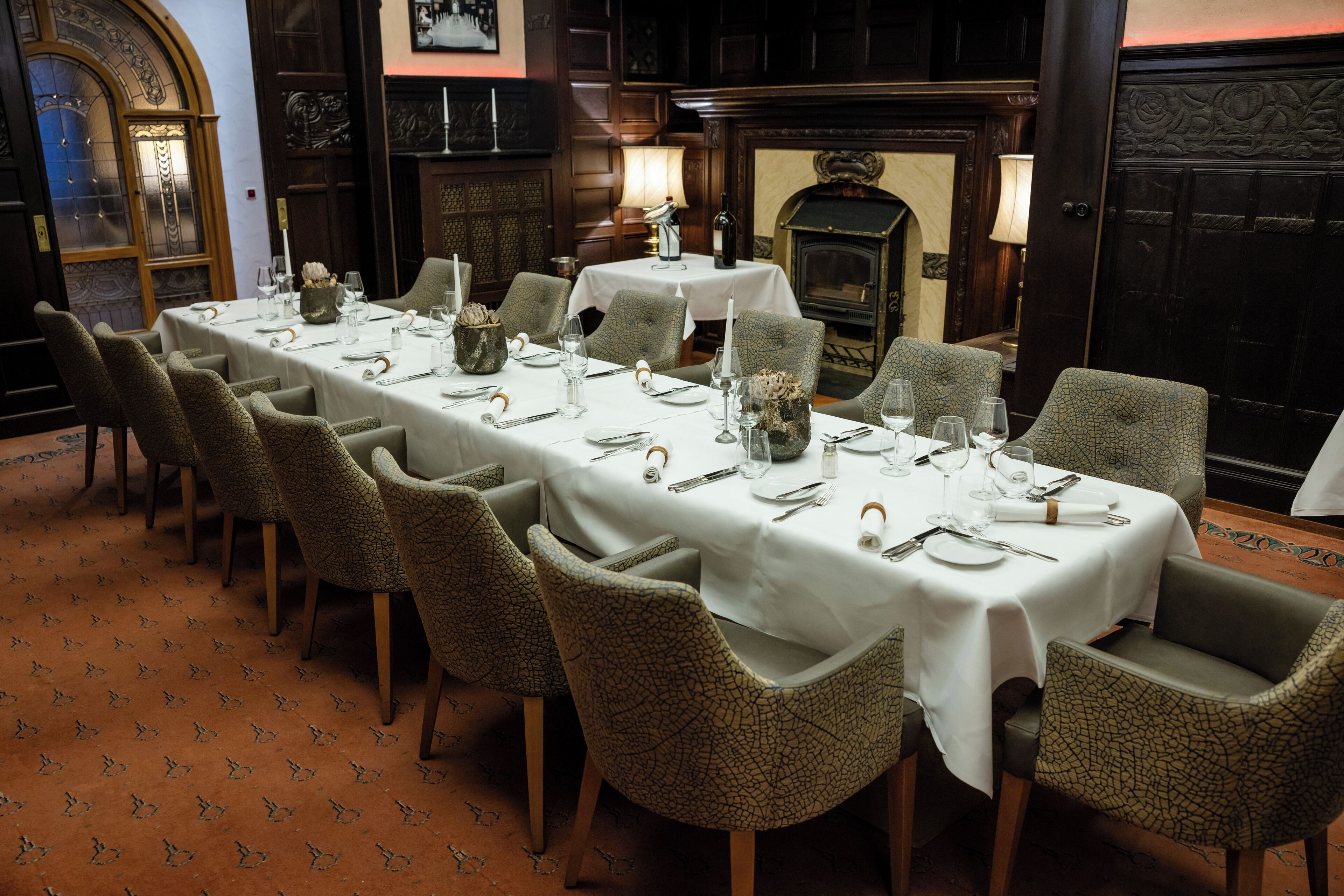 A long dining table set for six with chairs, a fireplace, and a clock on the wall.