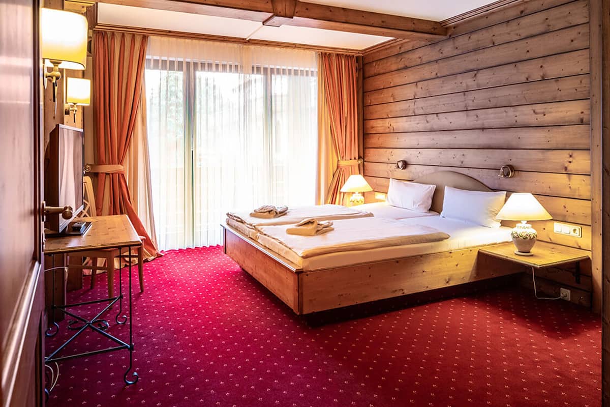 Hotelkamer met een houten hoofdeinde, twee bedden, een bureau met stoel, een televisie en een rode vloerbedekking.