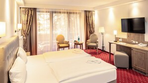 Habitación de hotel con una cama grande, dos sillas, un escritorio, un televisor y una ventana con cortinas.