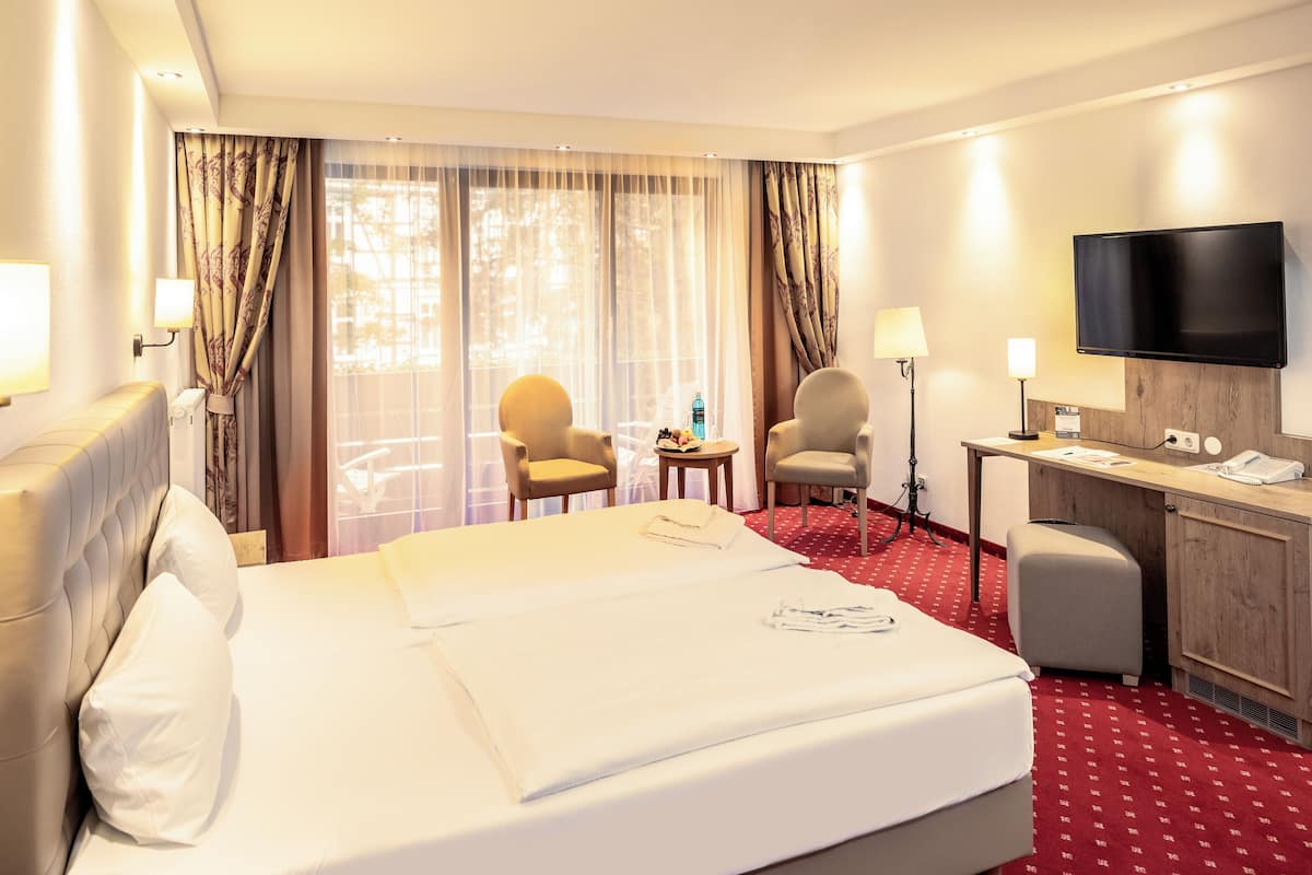 Een hotelkamer met een groot bed, twee stoelen, een bureau, een televisie en een raam met gordijnen.