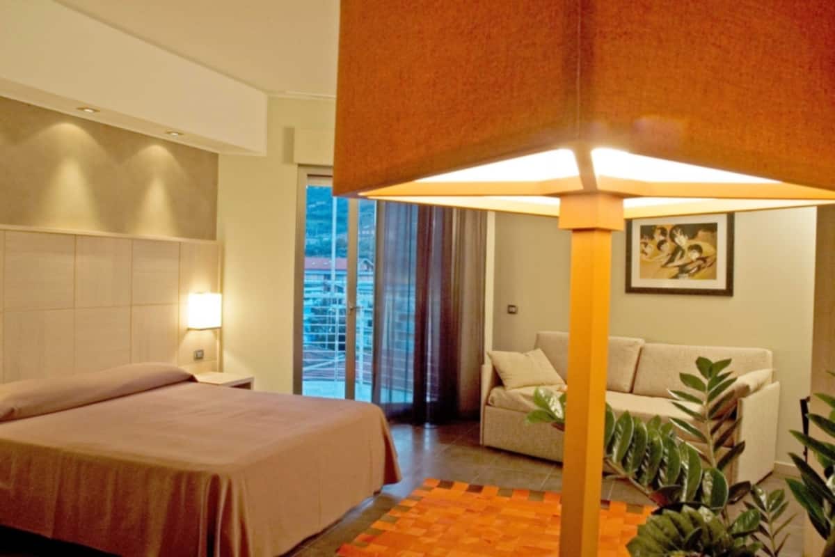 A hotel room with a bed, a sofa, a lamp, and a window with curtains.