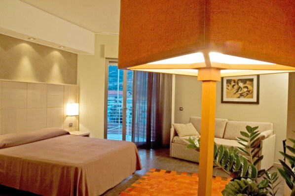 A hotel room with a bed, a sofa, a lamp, and a window with curtains.