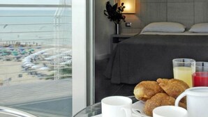 A hotel room with a bed, a table with breakfast items, and a view of a beach.