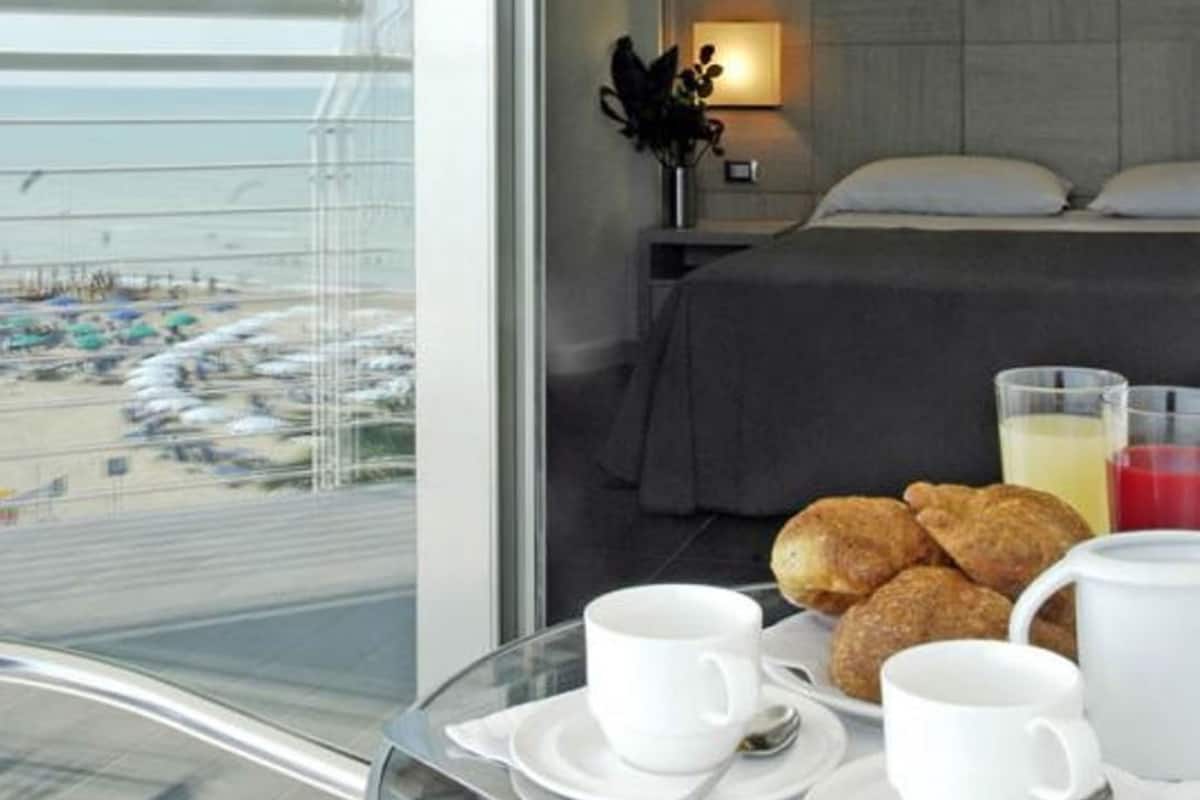A hotel room with a bed, a table with breakfast items, and a view of a beach.