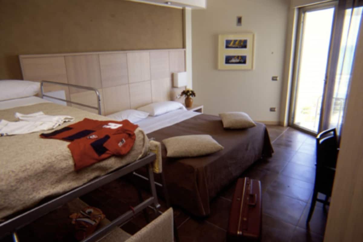 A hotel room with a bed, a bedside table, a chair, and a suitcase.