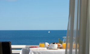 A table with breakfast items and a glass of orange juice, overlooking the sea.
