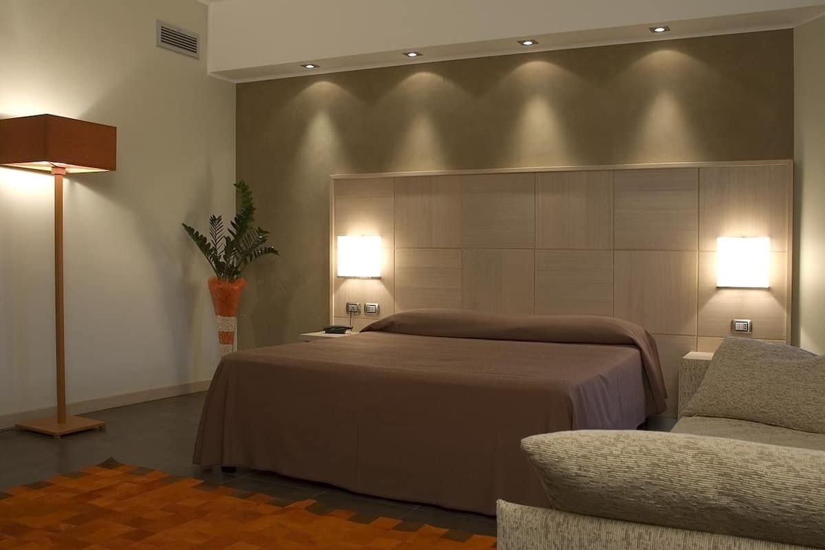 A modern bedroom with a large bed, bedside lamps, a floor lamp, and a decorative plant.