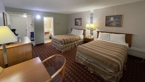 A hotel room with two beds, a desk, a chair, a lamp, and a bathroom visible through an open door. - The Autumn Inn (Bennington)