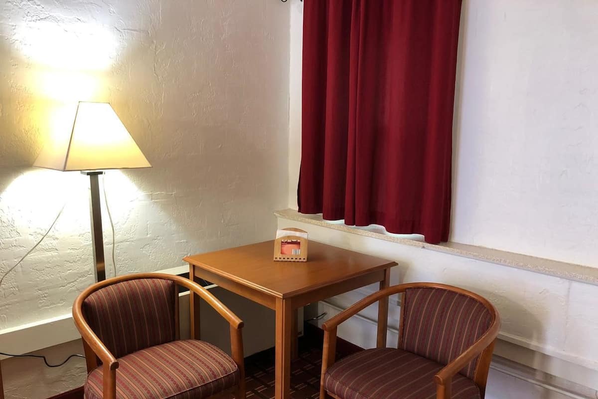 Una habitación pequeña con una mesa de madera y dos sillas a rayas, una lámpara y una ventana con cortinas rojas.