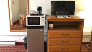 A compact room with a microwave, refrigerator, wooden dresser, and a television. - The Autumn Inn (Bennington)