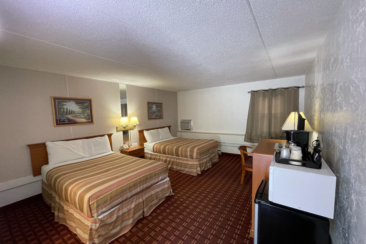 Habitación de hotel con dos camas, un escritorio, una silla, cafetera y televisor.