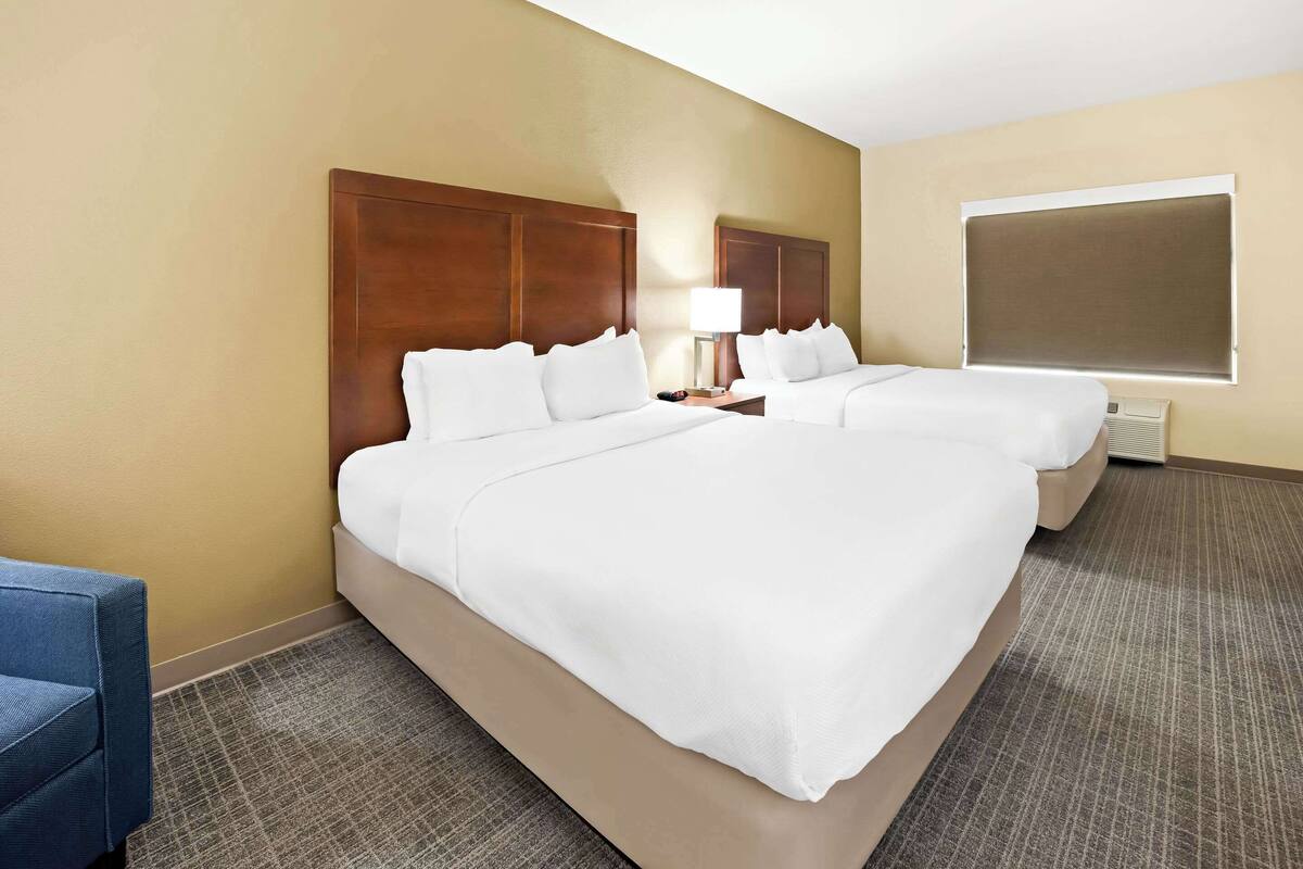 Une chambre d  ’hôtel avec deux lits, un bureau, une chaise et une fenêtre avec des stores.