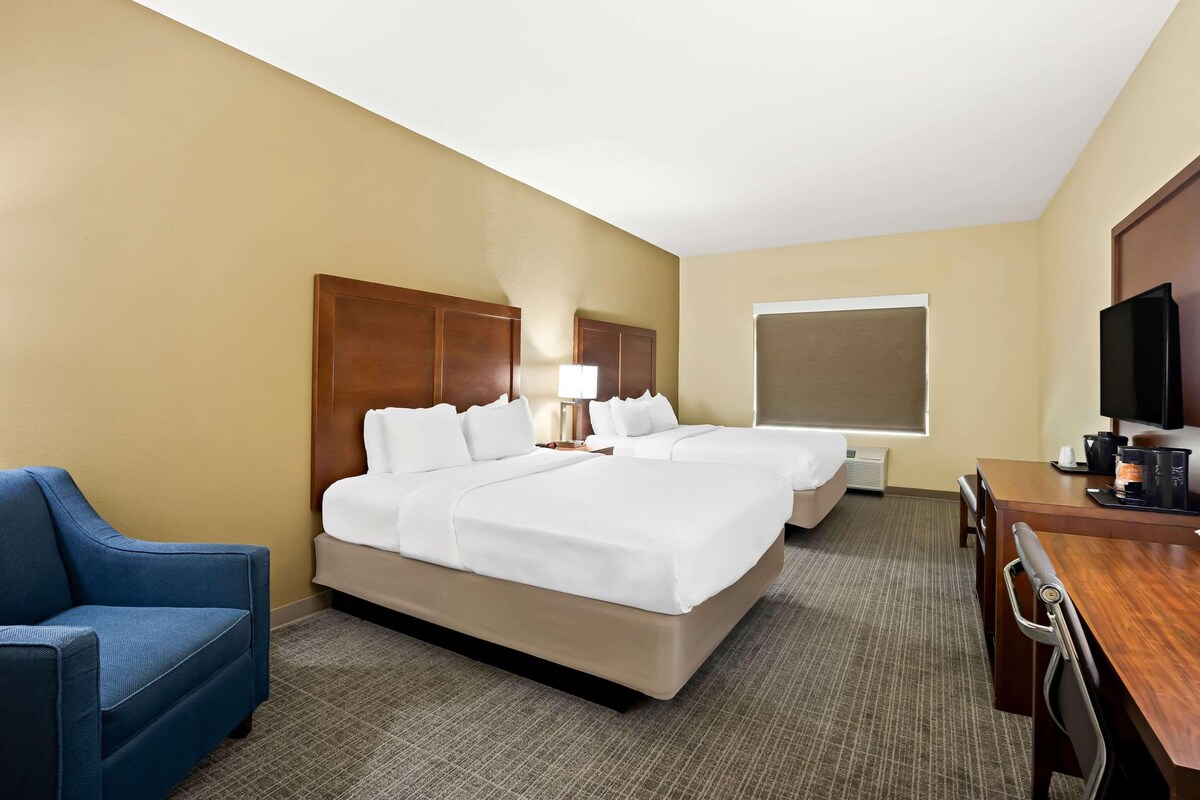 A hotel room with two beds, a desk, a chair, a television, and a window.