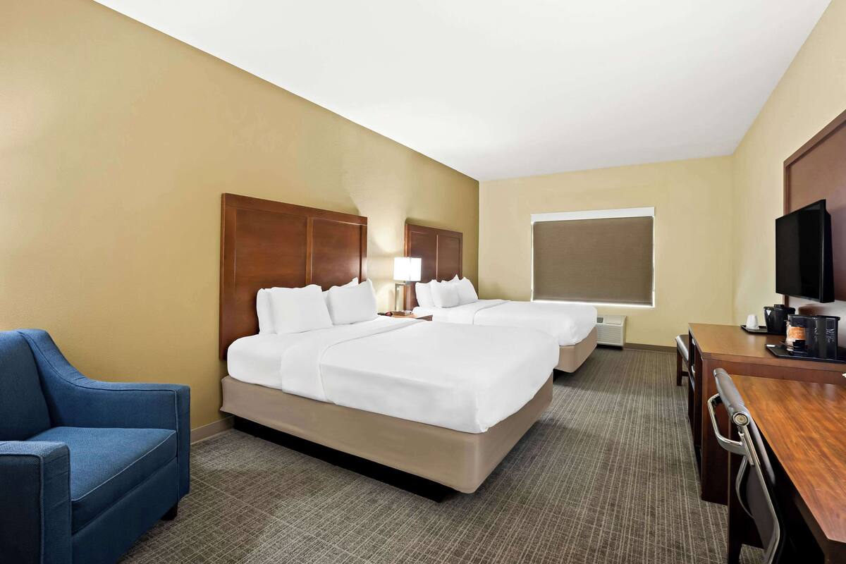 Une chambre d’hôtel avec deux lits, un bureau, une chaise et un téléviseur.