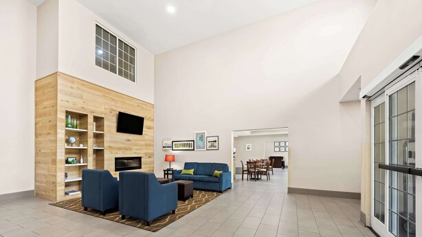 A spacious living area with a wooden accent wall, a blue sofa set, a flat-screen TV, and a dining area in the background. - Comfort Inn & Suites High Point - Archdale (High Point)