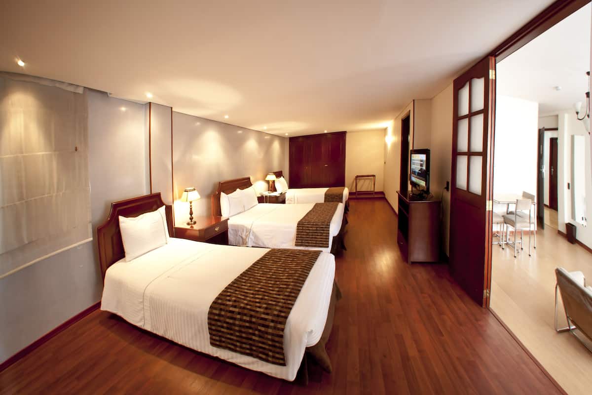A hotel room with two beds, wooden flooring, a large mirror, and a television.