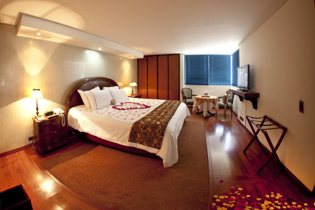 A hotel room with a bed, bedside table, lamp, chair, small table, and a TV.