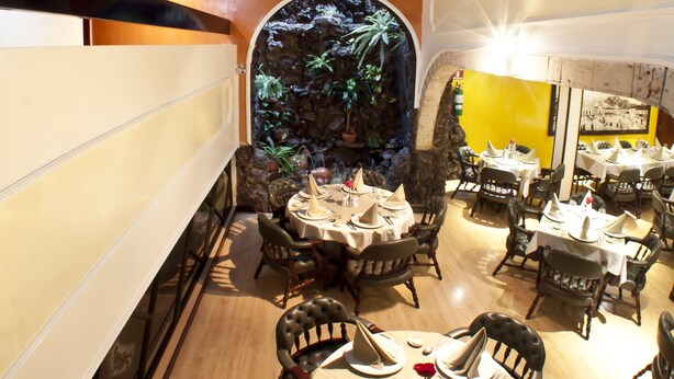 A restaurant with round tables, chairs, and a decorative wall with plants. - Hotel Centro Internacional (Bogotá)