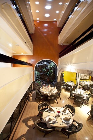 Un restaurante con mesas redondas, sillas y una pared decorativa con plantas.