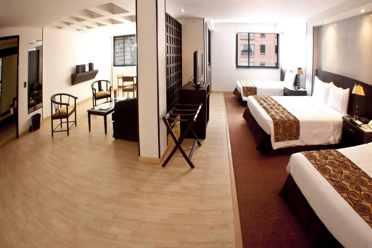 A hotel room with a bed, a desk, a chair, a TV, and a window with blinds.