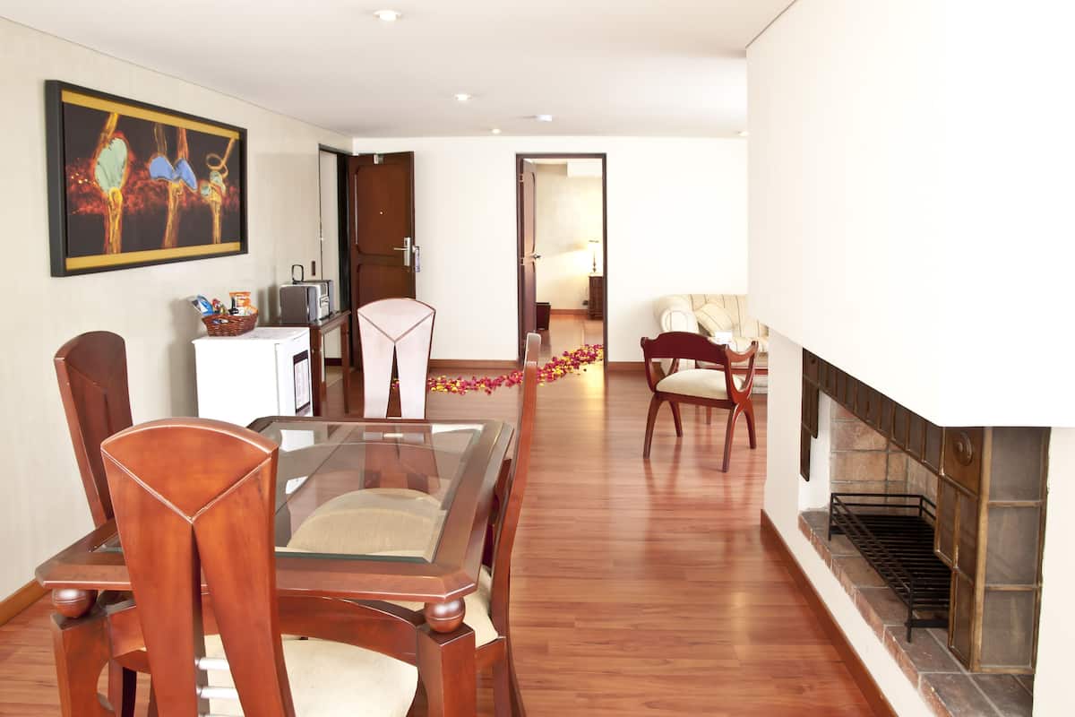 A dining area with a glass table and wooden chairs, a fireplace, and a painting on the wall.