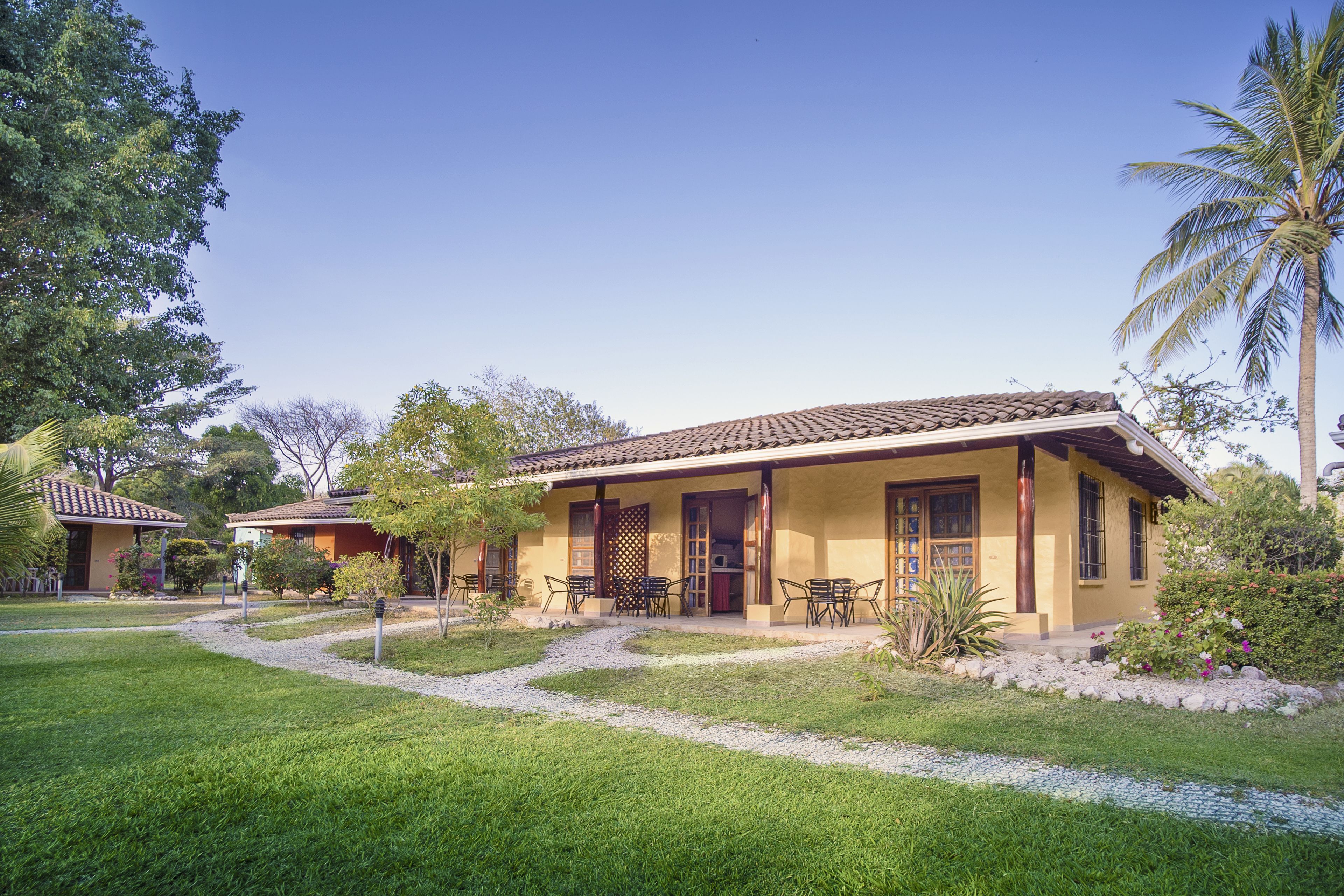 A two-story building with a tiled roof, a covered patio with outdoor furniture, and a well-maintained garden with a gravel path.