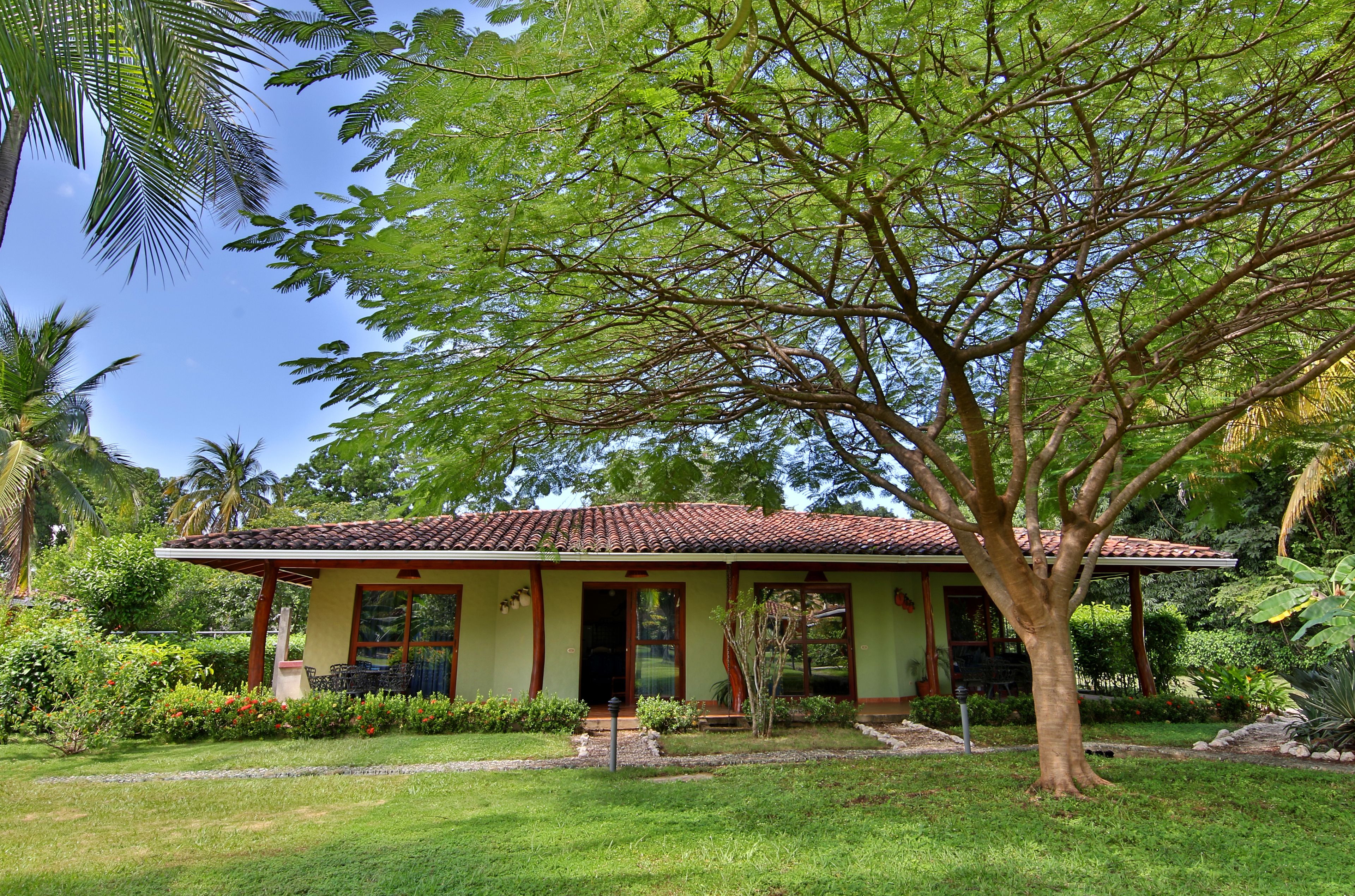 A house with a tiled roof, surrounded by lush greenery and a well-maintained lawn.