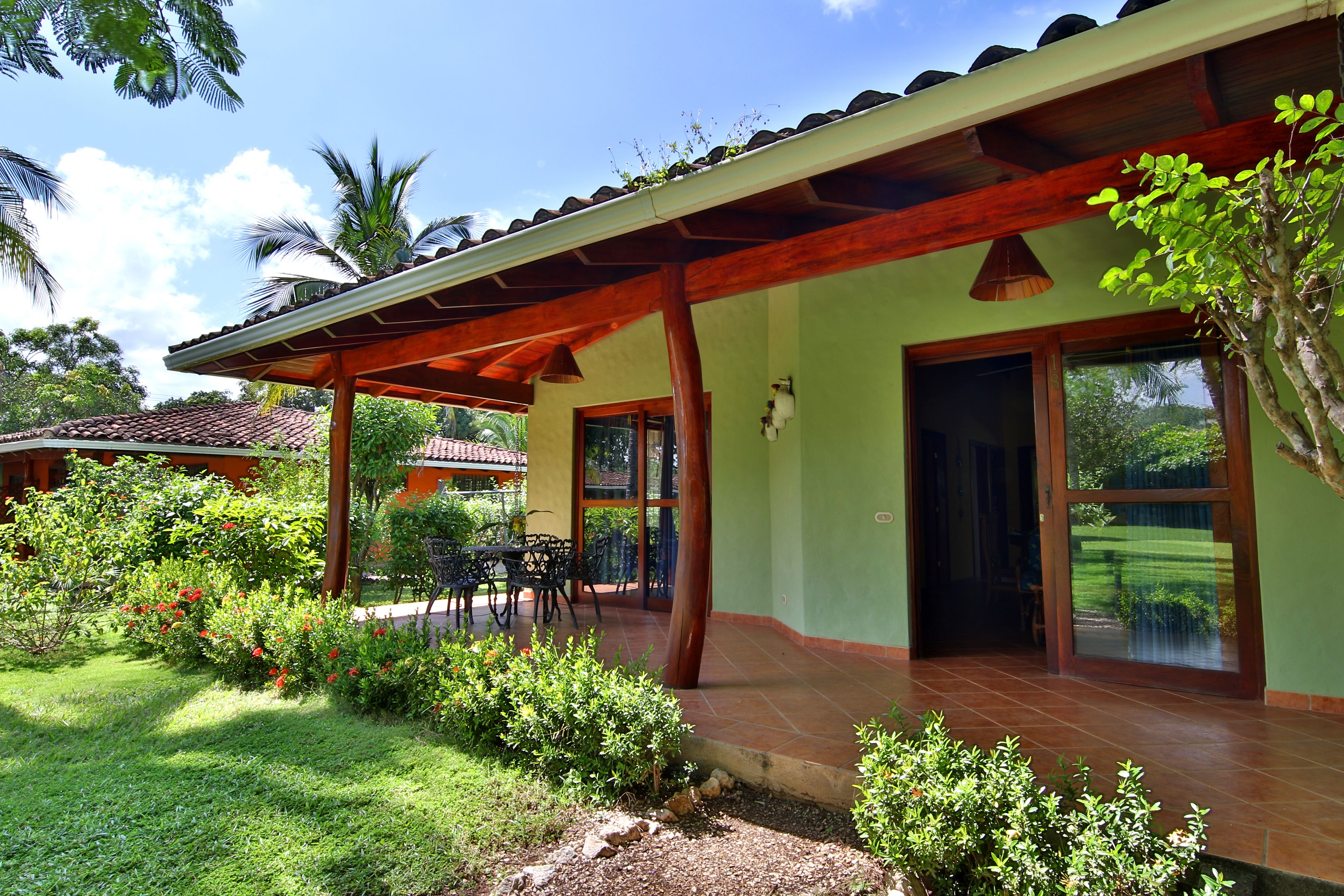 A house with a covered patio, a garden with various plants, and a view of the surrounding greenery.
