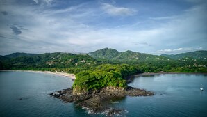 A coastal landscape with a small island surrounded by water, a beach, and a mountainous backdrop. - Bahia Esmeralda Boutique Hotel & Villas (Tempate)