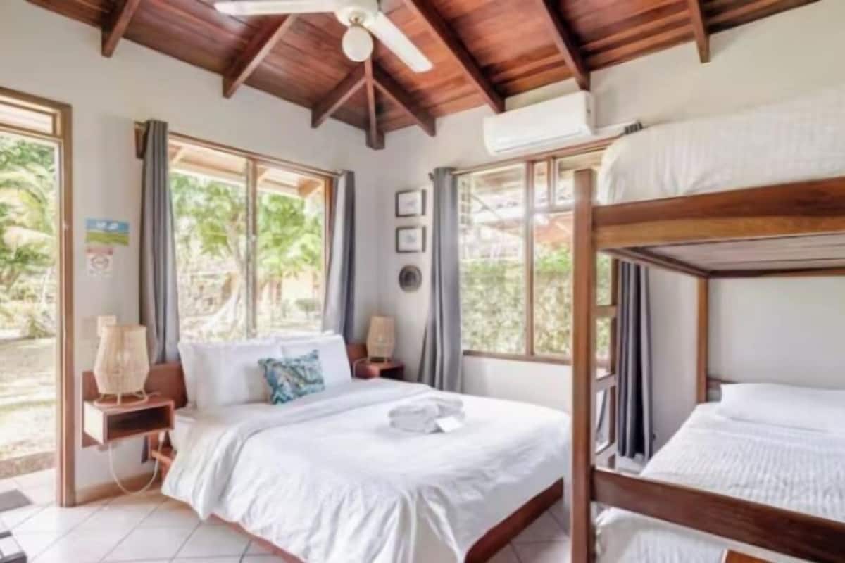 A bedroom with a wooden ceiling, a bed with white bedding, a bedside table, and a window with curtains.